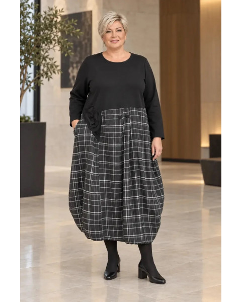 Женское комбинированное платье миди большого размера. Верхняя часть выполнена из гладкой черной ткани с длинным рукавом и круглым вырезом. Нижняя часть представляет собой объемную юбку-баллон в черно-белую клетку. На линии талии расположен декоративный тк